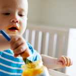toddler holding spoon playing with food