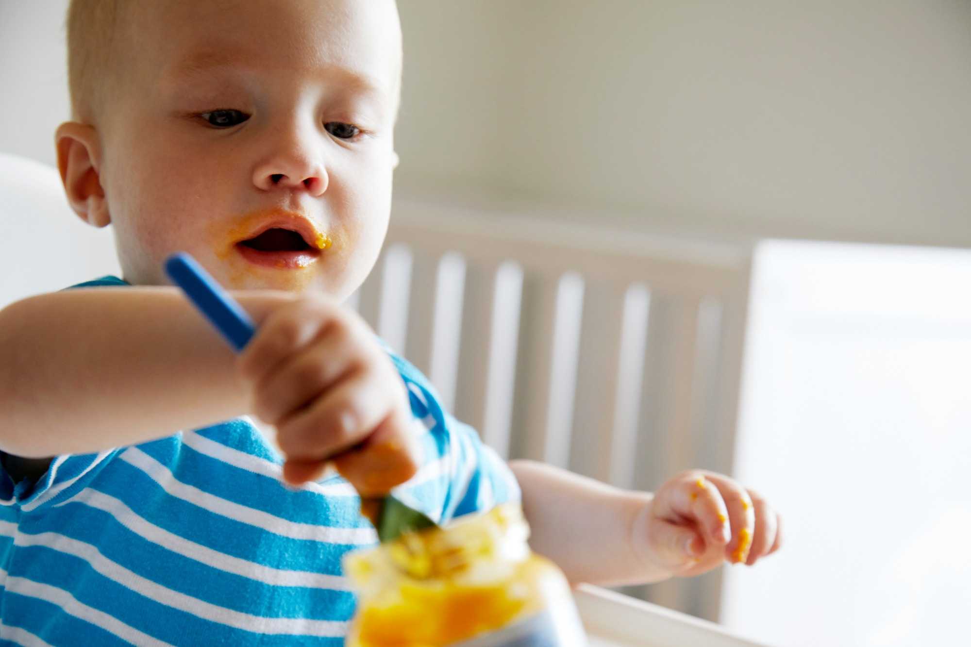 toddler holding spoon playing with food