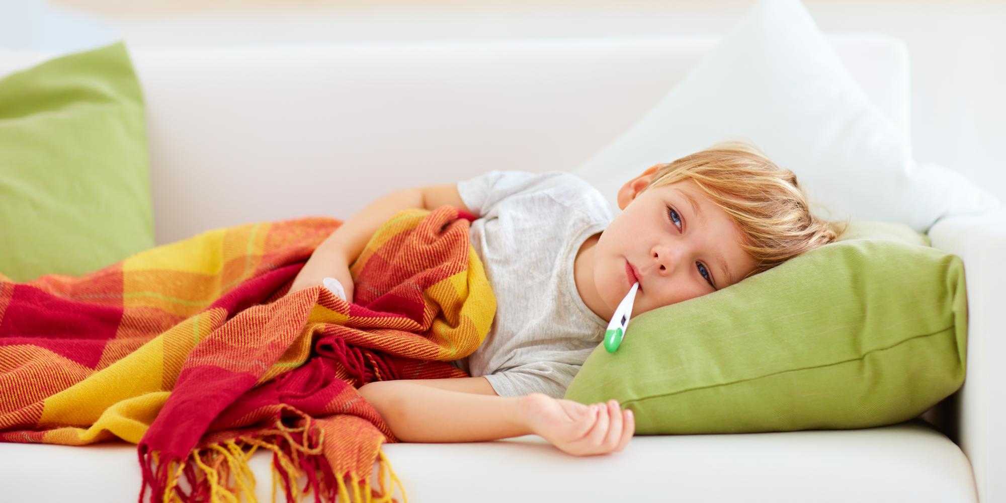 child on sofa with blanket and themometer in their mouth