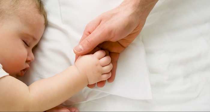 Sleeping baby holding fathers hand